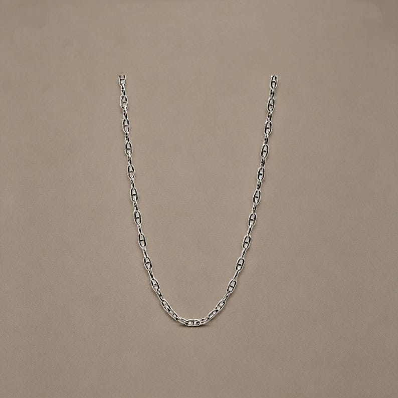 May include: A silver-toned chain necklace featuring a series of elongated, oval-shaped links, each reinforced with a central horizontal bar. The metallic links are interconnected to form a continuous, uniform chain design with a polished finish.