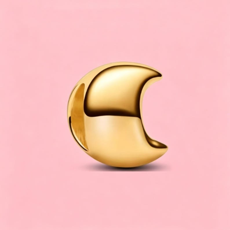 May include: A polished gold-tone metal charm shaped like a crescent moon. The charm features a smooth, reflective surface with a curved silhouette and a hollow opening on the side, designed for attachment to a bracelet or necklace chain.