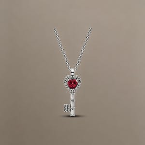 May include: A silver-toned necklace featuring a key-shaped pendant. The head of the key is a heart shape set with a vibrant red gemstone, surrounded by small clear stones. The shaft of the key is accented with baguette-cut clear stones.