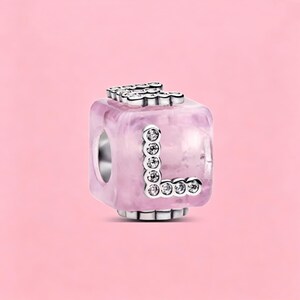 May include: A cube-shaped charm bead featuring a translucent light pink marbled resin body. The letter L is prominently displayed on the front face, outlined in silver-toned metal and inlaid with small, clear, sparkling round crystals.