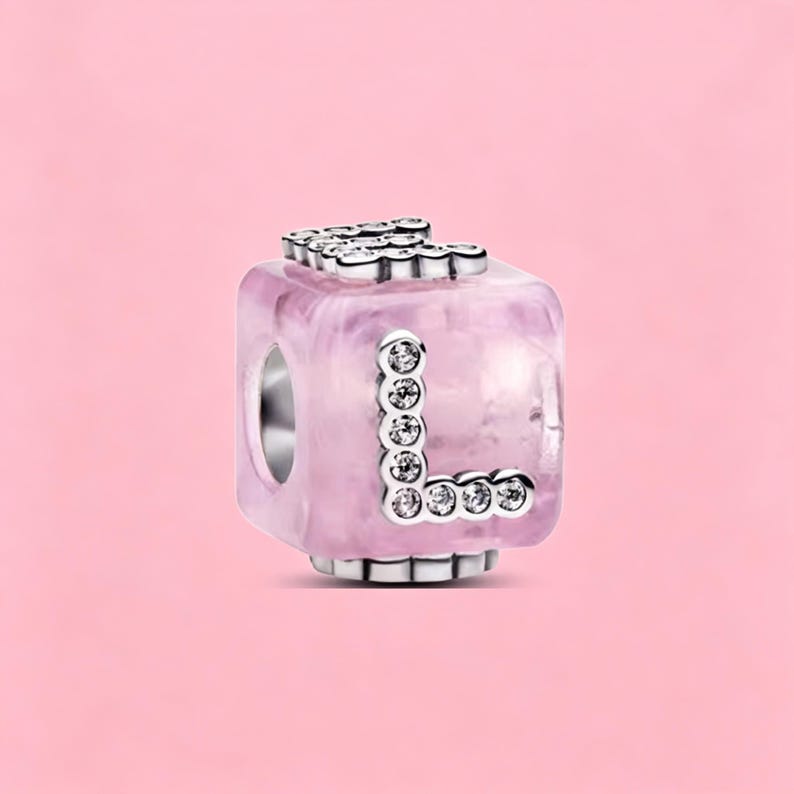 May include: A cube-shaped charm bead featuring a translucent light pink marbled resin body. The letter L is prominently displayed on the front face, outlined in silver-toned metal and inlaid with small, clear, sparkling round crystals.
