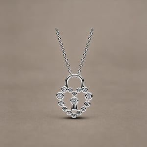 May include: A silver-coloured necklace featuring a heart-shaped padlock pendant. The pendant is outlined with small, clear, round-cut stones and includes a central keyhole design accented with a single stone, suspended from a delicate silver chain.