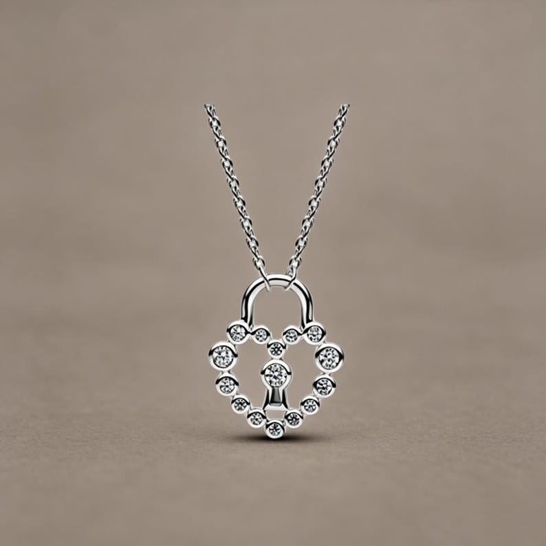 May include: A silver-coloured necklace featuring a heart-shaped padlock pendant. The pendant is outlined with small, clear, round-cut stones and includes a central keyhole design accented with a single stone, suspended from a delicate silver chain.
