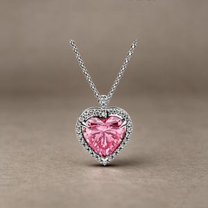 May include: A silver-toned necklace featuring a heart-shaped pendant with a large, faceted pink centre stone. The heart is surrounded by a halo of small, clear, sparkling stones set in metal, suspended from a delicate silver-toned chain.