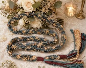 May include: A braided cord belt featuring teal and dark red threads interwoven with shimmering gold metallic accents. The belt ends in decorative tassels made of loose teal and dark red strands, accented with gold metallic fibers and knots.
