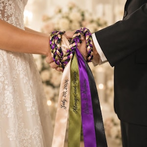 Może przedstawiać: Sznur do ceremonii handfasting z plecionymi satynowymi wstążkami w odcieniach fioletu, zieleni, czerni i szampana. Trzy długie wstążki zwisają w dół, wyhaftowane tekstem July 20, 2026, Always and Forever oraz Elian & Madison czcionką.