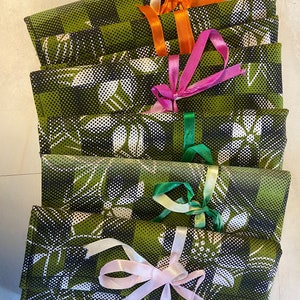 Puede incluir: Una pila de seis bolsas de regalo de tela verde con patrones florales negros y blancos. Cada bolsa está atada con una cinta de color diferente: naranja, rosa, verde y rosa.