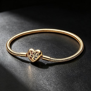 Könnte beinhalten: Ein goldfarbenes Schlangenkettenarmband mit einem herzförmigen Verschluss. Der Verschluss ist mit einem komplexen Lebensbaum-Motiv verziert, das kleine, klare, funkelnde Steine enthält, die in die Äste des Baumdesigns eingearbeitet sind.