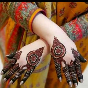 May include: Two hands decorated with intricate dark brown henna patterns featuring central circular mandala designs on the back of each hand, surrounded by detailed geometric lines, dots, and floral motifs extending down to the fingertips.