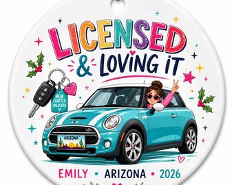 May include: A round white ceramic ornament featuring a teal car with white stripes, a person inside making a peace sign, and a car key with a tag reading NEW CHAPTER UNLOCKED. Text reads LICENSED & LOVING IT, EMILY, ARIZONA, and 2026 with holly and stars.