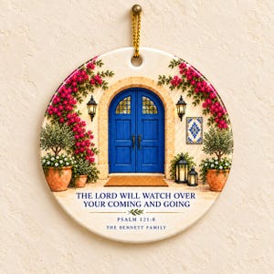 Peut inclure: Un ornement en céramique rond illustrant une entrée à double porte bleue avec des fleurs roses, des plantes en pot et des lanternes. Le texte indique : THE LORD WILL WATCH OVER YOUR COMING AND GOING, PSALM 121:8, THE BENNETT FAMILY. Il est suspendu par un cordon doré.