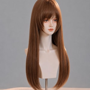Puede incluir: Un maniquí de cabeza de muñeca con cabello largo y liso de color marrón, mechones en capas que enmarcan el rostro y flequillo recto. La muñeca tiene una tez pálida, ojos marrones pintados y labios de color rosa claro, sobre un soporte de metal.