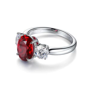Anillo de compromiso ovalado con rubí sintético, detalles de moissanita y tres piedras en plata de ley.