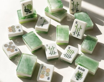 May include: A collection of rectangular mahjong tiles featuring a white top surface with green, black, and orange ink illustrations of numbers, bamboo stalks, circles, a peacock, and a dragon, paired with a translucent green marbled base.