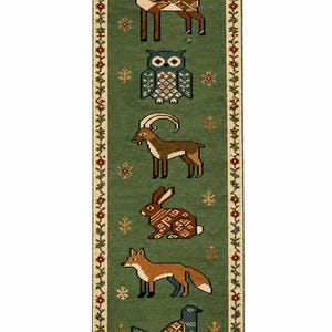 Op de afbeelding: Een rechthoekig groen loperkleed met een reeks van zes gestileerde dieren, waaronder een hert, uil, steenbok, konijn, vos en vogel. Het kleed heeft een crèmekleurige rand met een bloemmotief en franjes aan beide uiteinden met kleine sneeuwvlokken.