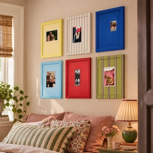 May include: A gallery wall arrangement of six rectangular picture frames in yellow, white with black stripes, blue, light blue, red, and green with purple stripes, each containing a photograph, displayed above a bed with patterned pillows.