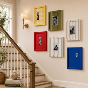 May include: A gallery wall arrangement featuring six rectangular picture frames in yellow, olive green, red, white with black stripes, white with dark green stripes, and blue. Each frame contains a black and white photograph or patterned insert.