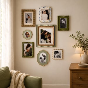 May include: A gallery wall arrangement featuring eight assorted picture frames in various shapes and colors, including olive green beaded frames, a floral patterned frame, a striped frame, and scalloped gold-rimmed frames displaying photographs.