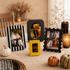 May include: Four decorative picture frames in various styles and colors, including a black and white striped frame, a solid black oval frame, a small yellow ornate frame, and a black scalloped frame, all displaying Halloween-themed photographs.