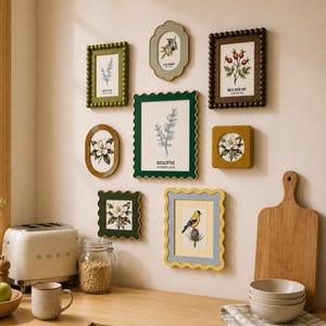 May include: A gallery wall arrangement featuring eight assorted picture frames in various shapes and colors, including scalloped and beaded edges. The frames contain botanical and bird illustrations with text labels like Eucalyptus, Olive Branch, and Wild Rose Hip.