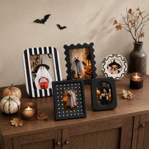 May include: A collection of five picture frames featuring various designs including black and white stripes, scalloped edges, and a star pattern. The frames display photographs of individuals and pets in Halloween costumes, arranged with pumpkins and candles.