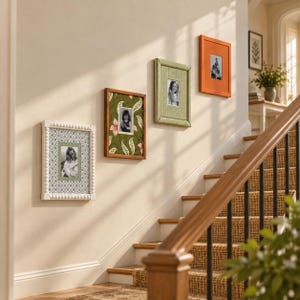 May include: Four rectangular wall-mounted picture frames arranged in a diagonal line. The frames feature distinct designs: a white beaded frame, a wooden frame with a green floral mat, a ribbed green frame, and a solid orange frame.