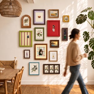 May include: A gallery wall arrangement featuring various rectangular and arched picture frames in colors including red, green, brown, and blue. The frames contain diverse botanical illustrations, landscape prints, and photographs on a plain wall.