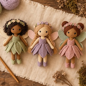 May include: Three handmade crochet dolls featuring fairy wings and floral crowns. The left doll has dark curly hair and a sage green dress. The centre doll has blonde braided hair and a lavender dress. The right doll has brown hair and a dusty rose dress.