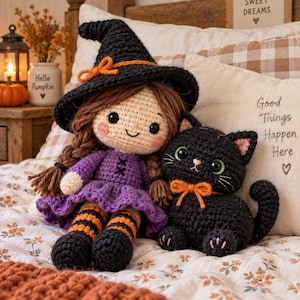 May include: A crocheted doll wearing a black witch hat with an orange bow, a purple dress, and orange and black striped stockings, sitting next to a small black crocheted cat with green eyes and an orange bow around its neck.