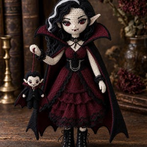 May include: A handcrafted crochet doll featuring a vampire character with black hair, red eyes, and pointed ears. The doll wears a dark red dress with black lace trim, a black cape with a high collar, and black boots. It holds a small matching vampire doll.