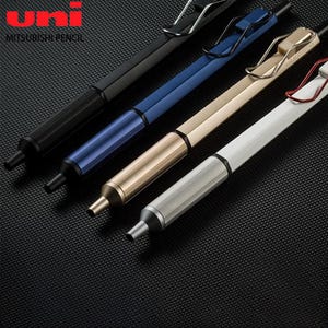 Może przedstawiać: Cztery ołówki automatyczne Uni Mitsubishi Pencil ułożone po przekątnej. Długopisy mają sześciokątny korpus z teksturowaną sekcją uchwytu i metalowym klipsem do kieszeni. Kolory to matowa czerń, metaliczny błękit, metaliczne złoto i srebro.