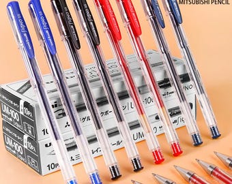 May include: A collection of Uni-ball Signo 0.5 gel pens in blue, black, and red, featuring clear plastic barrels and matching colored caps with clips. The pens are displayed alongside stacked boxes labeled UM-100 and Mitsubishi Pencil.
