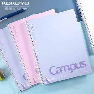 May include: Three spiral-bound B5 notebooks in light purple and pink, featuring the text Campus and Kokuyo. Each notebook has a white wire-o binding along the left side, a printed grid pattern on the cover, and a small triangular graphic detail.