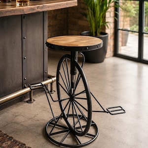 May include: A bar stool featuring a round wooden seat atop a black metal base designed to resemble a bicycle wheel. The structure includes a central vertical support with a screw mechanism for height adjustment, two pedals, and a circular base.