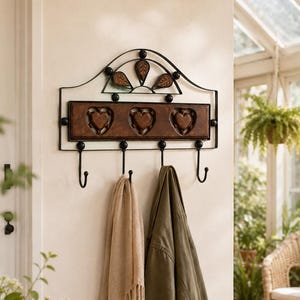 May include: A black metal wall-mounted coat rack featuring a rectangular wooden panel with three carved heart shapes. The rack includes four curved hooks for hanging items, topped with a decorative arched metal frame with leaf-shaped accents.