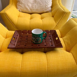 Pu&ograve; includere: Un vassoio rettangolare in legno marrone scuro con superficie intrecciata e manici intagliati, che sostiene una tazza in ceramica verde con la scritta "TURKIYE" e varie illustrazioni grafiche stampate, appoggiato su una poltrona giallo brillante.