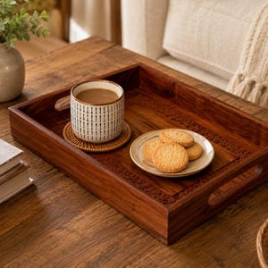 May include: A rectangular wooden serving tray with carved floral details along the inner edges, featuring integrated side handles. The tray holds a ceramic mug with a vertical dash pattern filled with coffee and a small plate with three cookies.