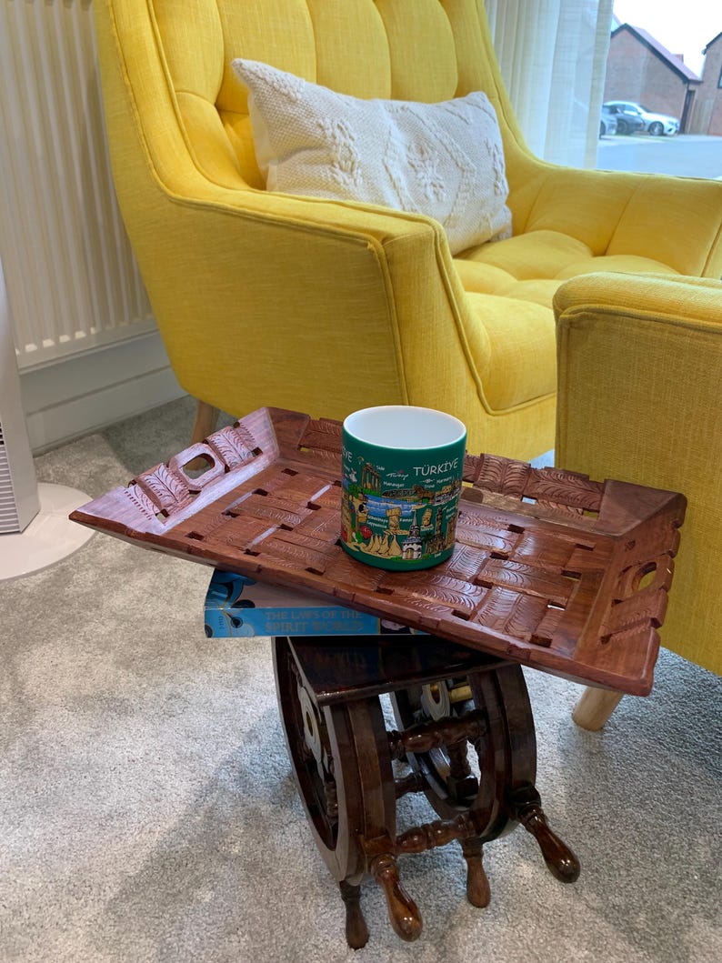 Pu&ograve; includere: Un vassoio rettangolare in legno con superficie intrecciata e manici intagliati, con sopra una tazza in ceramica verde decorata con una stampa grafica colorata di monumenti e la scritta T&Uuml;RKIYE, poggiato su un tavolino in legno scuro.