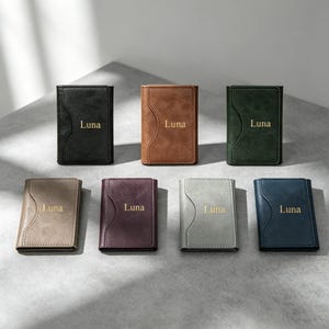 May include: Seven rectangular wallets arranged in two rows, featuring a curved stitched detail on the front. Each wallet is a different color—black, brown, dark green, beige, maroon, gray, and navy—and displays the name Luna in gold lettering.