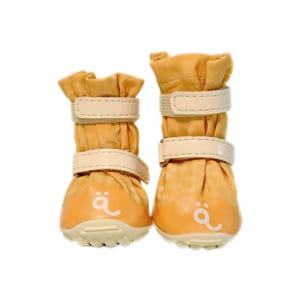 May include: A pair of mustard yellow pet boots featuring two beige hook-and-loop straps on each shaft. The boots have a rounded toe cap with a white graphic symbol resembling a stylized letter a with two dots above it and a textured sole.