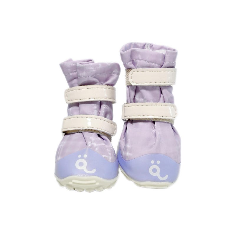 May include: A pair of light purple pet boots featuring two white hook-and-loop straps across the front. The boots have a solid light purple toe cap with a white logo printed on the front and a textured white sole for traction and stability.