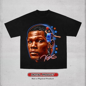 May include: A black t-shirt featuring a large graphic print of a basketball player's face, a smaller action shot of the player in a blue jersey, orange and blue stars, and a signature. The text reads DIGITAL PRODUCT Not a Physical Product.