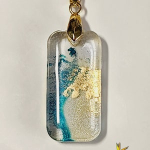 May include: A gold chain necklace with a rectangular glass pendant. The pendant contains blue and gold flecks inside the clear glass.