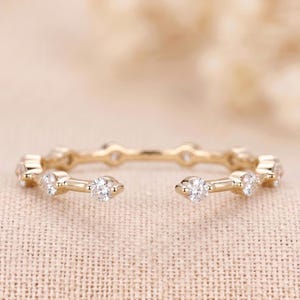 May include: A gold open-style ring featuring a series of small, round, clear faceted stones set along the band. The ring has a polished metallic finish and a gap at the front, with the stones spaced evenly around the circular band structure.