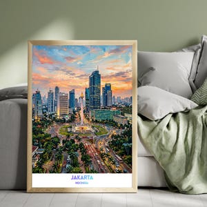 Può includere: Una stampa artistica verticale incorniciata che raffigura lo skyline di Giacarta al tramonto, con il Monumento Nazionale circondato da grattacieli, alberi e strade trafficate. Il testo "JAKARTA INDONESIA" è stampato in blu e nero in basso.