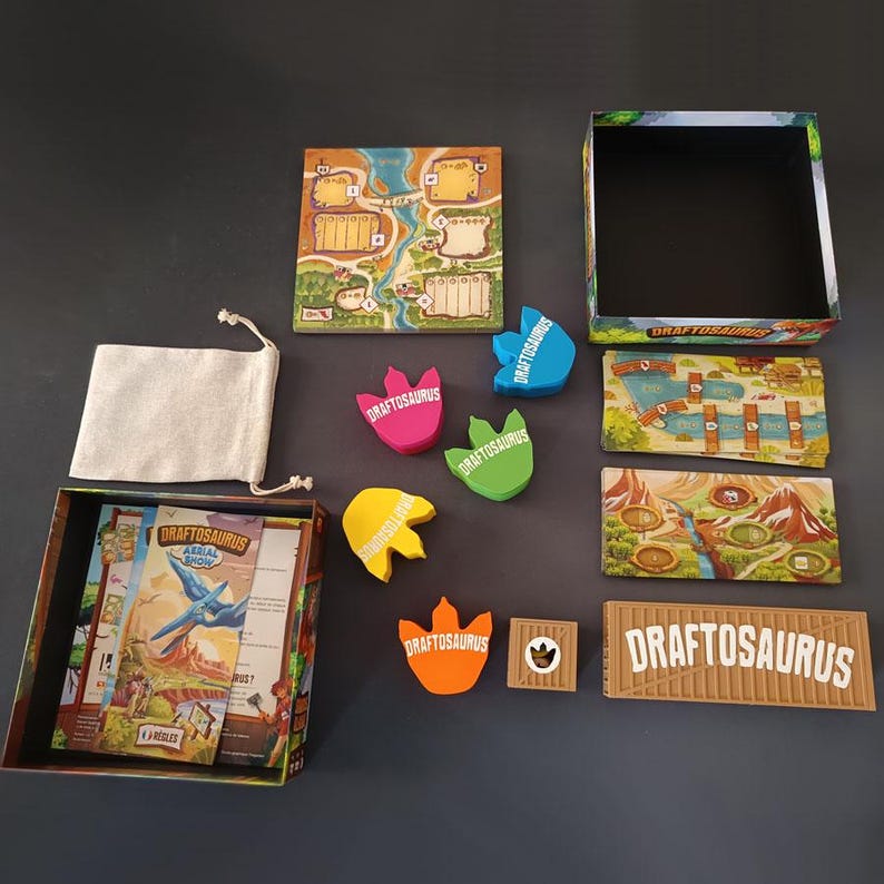Pode incluir: Um conjunto de jogo de tabuleiro incluindo uma caixa, um tabuleiro quadrado, um saco de tecido bege com cord&atilde;o e v&aacute;rias fichas coloridas em forma de dinossauro com a etiqueta Draftosaurus. Inclui tamb&eacute;m cartas retangulares e pe&ccedil;as de jogo.