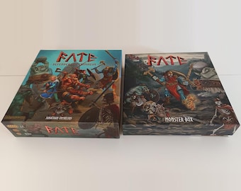 Pode incluir: Duas caixas retangulares de jogos de tabuleiro intituladas FATE. A caixa da esquerda está rotulada como Defenders of Grinheim por Jonathan Fryxelius, com personagens de fantasia em batalha. A caixa da direita diz Monster Box.