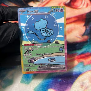 May include: A Mew ex trading card featuring a blue Mew character inside a circular bubble on a light blue and green background. The card displays the text Mew ex, 180 HP, Ability Restart, and Genome Hacking, with a holographic finish and card number 232/091.