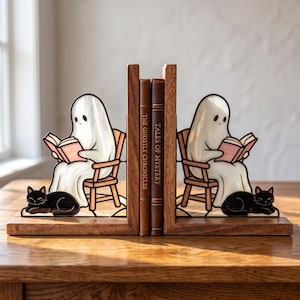 May include: A pair of wooden bookends featuring two white ghosts sitting in chairs and reading pink books, with a black cat lying at the feet of each ghost. The bookends support two brown books titled The Ghostly Chronicles and Tales of Mystery.