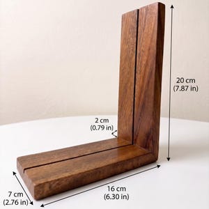 Puede incluir: Un soporte de exhibici&oacute;n de madera en forma de L con una ranura vertical, que mide 20 cm de altura, 16 cm de longitud y 2 cm de ancho. El soporte presenta un acabado de grano de madera marr&oacute;n natural y un dise&ntilde;o angular limpio para sostener objetos.
